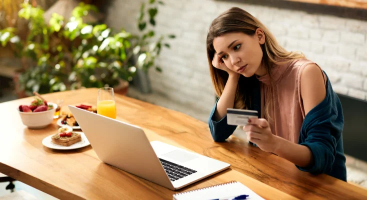 young woman feeling sad while checking her online bank account laptop home